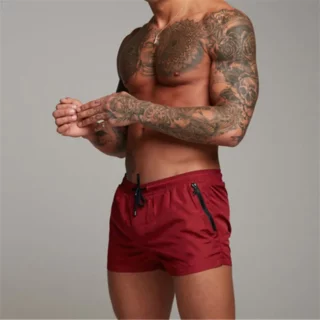 On voit un homme tatoué qui porte un maillot de bain style boxer de bain, rouge.
