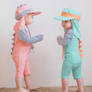 On voit deux bébés qui portent des maillots de bain en forme de dinosaure roses et bleu, avec des chapeaux assortis.