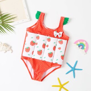 On voit un maillot de bain une pièce avec des flotteurs pour petite fille. Il est rouge avec les flotteurs en ceinture blancs imprimé fraises.