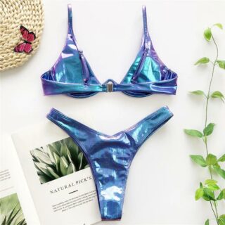 Photo d'un maillot de bain irisé bleu deux pièces à armatures et slip brésilien sur fond avec chapeau à gauche, livre sous le slip, et branche de plante à droite