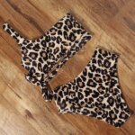 Photo d'un maillot de bain léopard 2 pièces avec un haut asymétrique à une brettelle et une culotte haute, posé sur du parquet