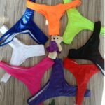 Photos représentant des strings de bain de huit couleurs différentes en rond sur fond bois avec petit ours en peluche au centre