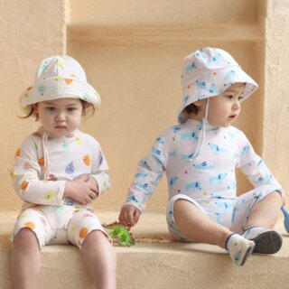 On voit deux bébés assis sur un muret qui portent des maillots de bain anti UV avec chapeaux assortis. L'un est blanc avec des motifs orange et jaunes, l'autre est blanc avec des motifs bleus.