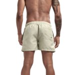 On voit un homme tatoué de dos, qui porte un short de bain beige respirant très simple.