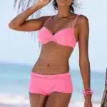 Photo d'une femme debout dos à la mer portant un maillot de bain shorty rose et un bracelet assorti