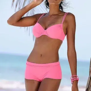 Photo d'une femme debout dos à la mer portant un maillot de bain shorty rose et un bracelet assorti