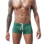 Photo d'un homme debout portant un maillot de bain shorty moulant vert foncé le tout sur fond blanc